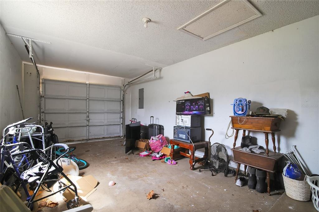 A cluttered garage features a white sectional door, concrete flooring, and various stored household items — 8779 SE 89TH PLACE, OCALA, FL