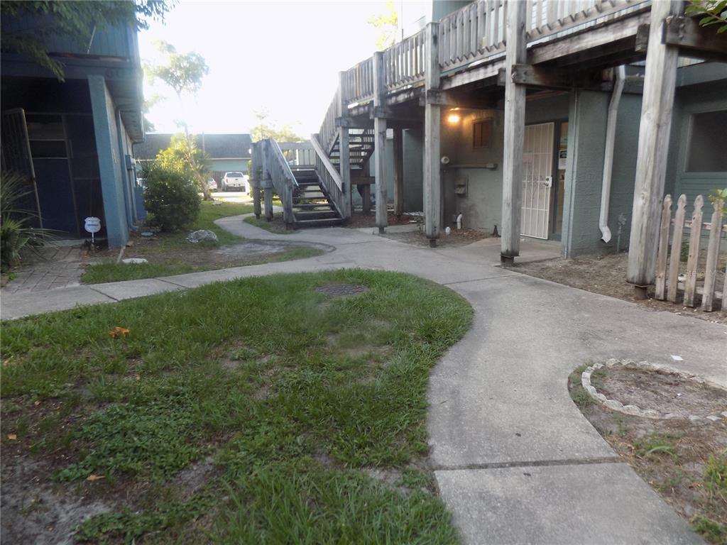 An outdoor view of a multi-story apartment building with wooden stairs and a concrete walkway — 613 SW 75 STREET UNIT 101, GAINESVILLE, FL