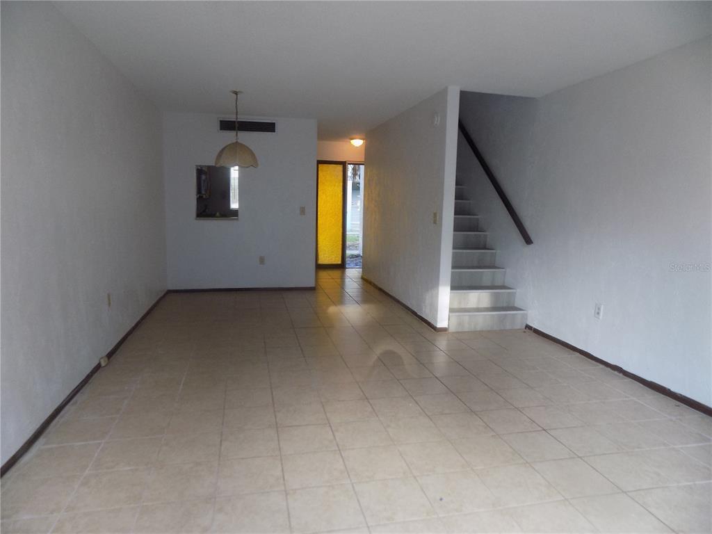 An empty room with light-colored tile flooring, white walls, and a staircase leading upstairs — 613 SW 75 STREET UNIT 101, GAINESVILLE, FL