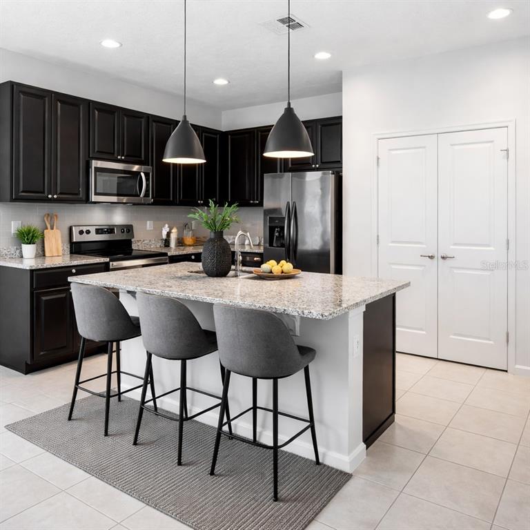 A kitchen features dark cabinets, granite countertops, a central island with bar seating, and stainless appliances — 213 TRINITY RIDGE CIRCLE, DAVENPORT, FL