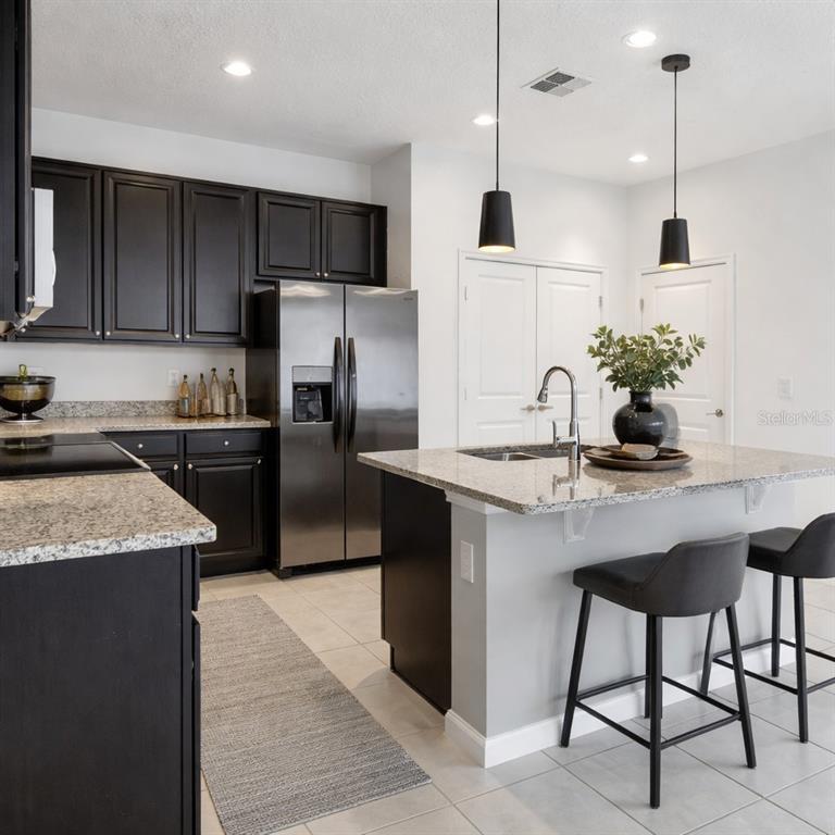 A kitchen features dark cabinets, granite countertops, a stainless steel refrigerator, and a center island — 213 TRINITY RIDGE CIRCLE, DAVENPORT, FL