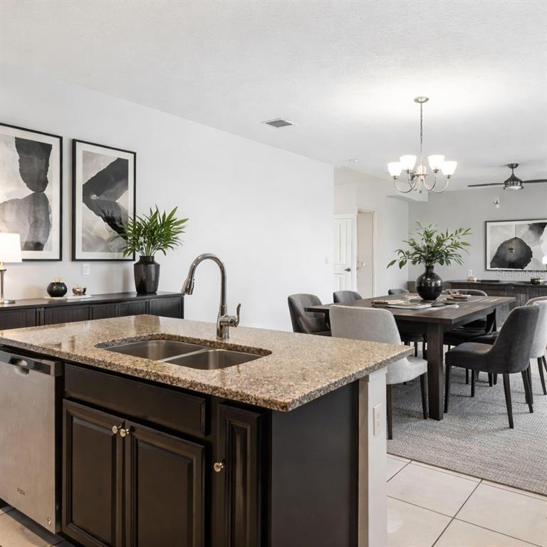 A kitchen island with a granite countertop and sink overlooks a dining area — 213 TRINITY RIDGE CIRCLE, DAVENPORT, FL