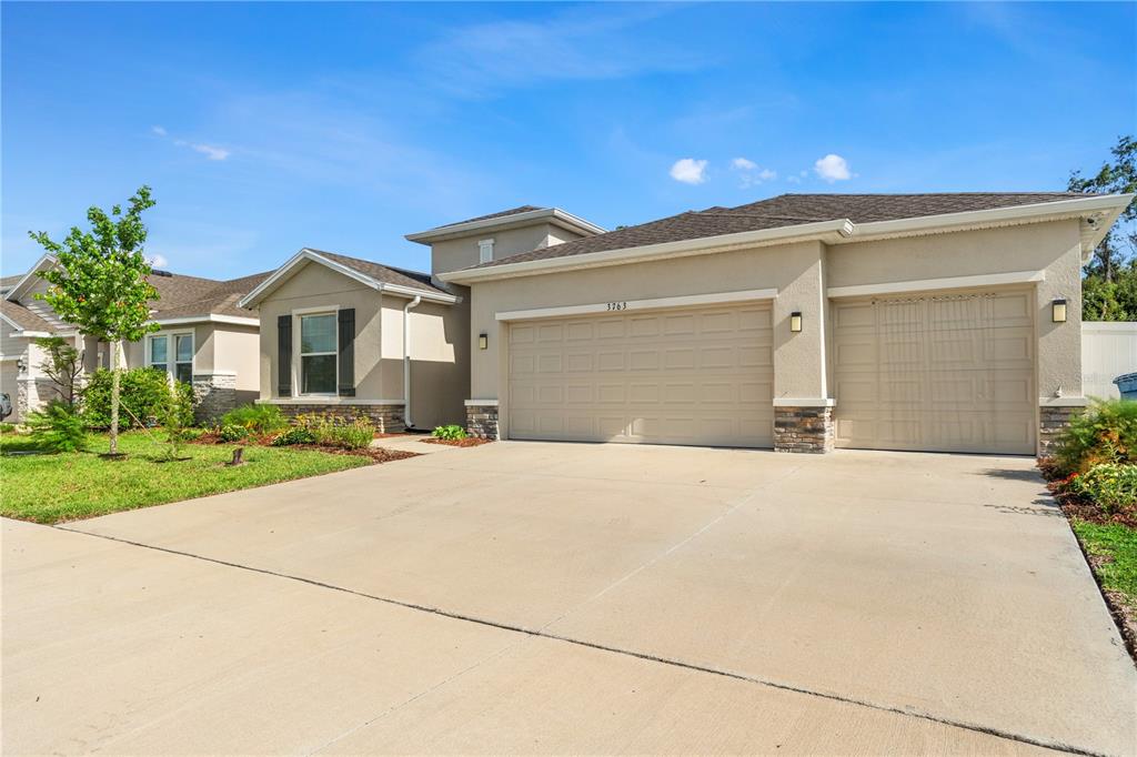 A beige, single-story suburban house features a three-car garage and a concrete driveway — 3763 AUTUMN AMBER DRIVE, SPRING HILL, FL