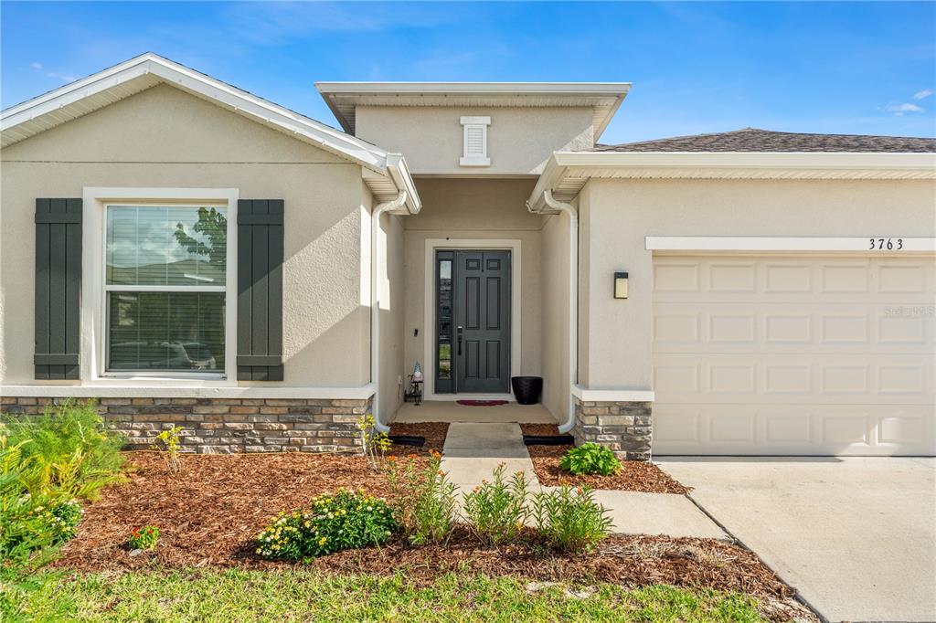 A single-story house exterior features a tan stucco facade, stone accents, and a dark front door — 3763 AUTUMN AMBER DRIVE, SPRING HILL, FL