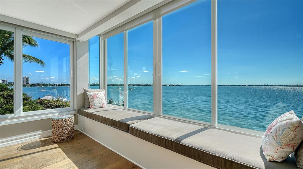 A sunroom features a long window seat with cushions overlooking a bay with boats — 400 GOLDEN GATE POINT UNIT 31, SARASOTA, FL