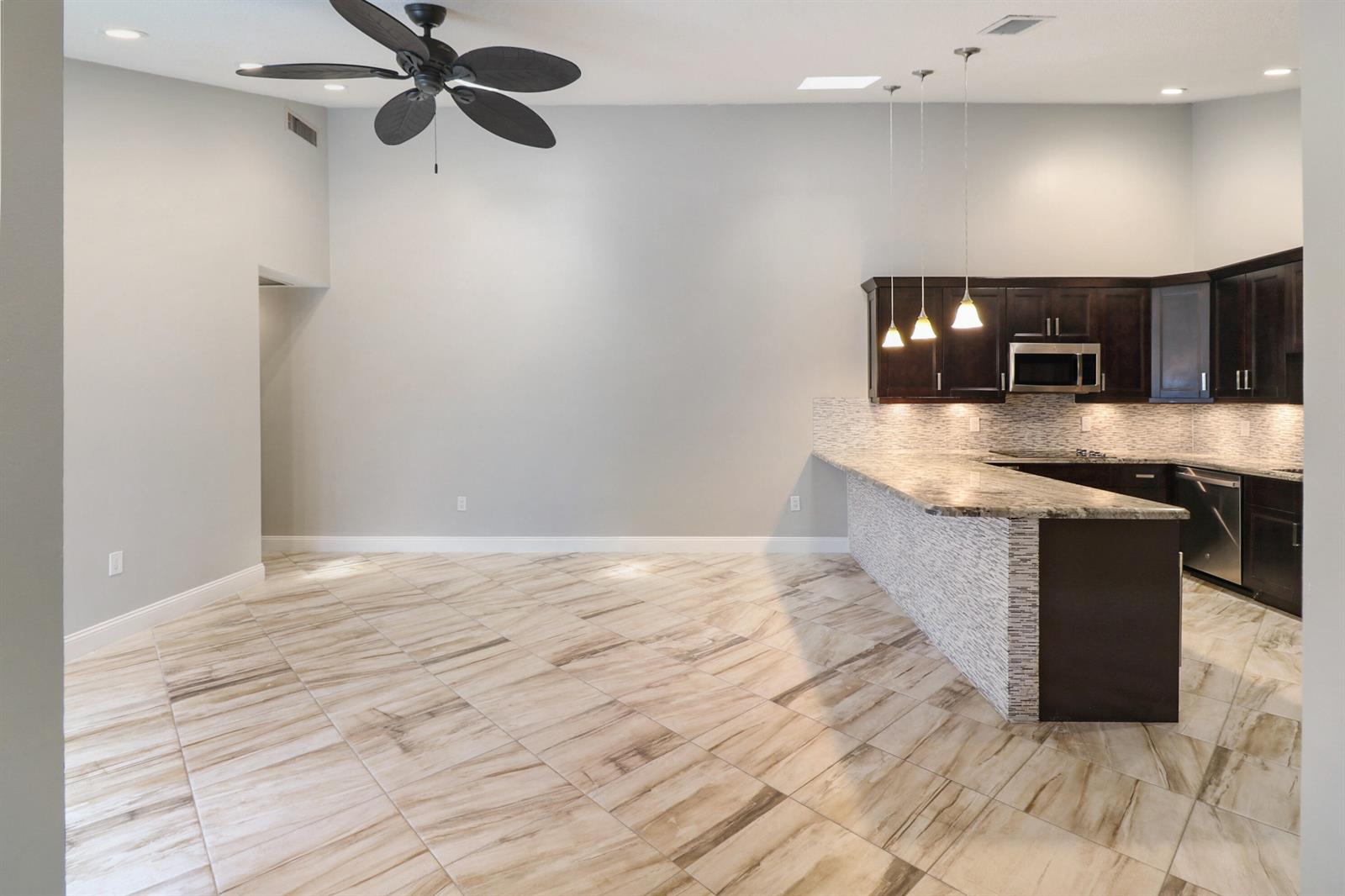 An open-concept kitchen with dark cabinets, granite countertops, and tile flooring — 9713 Boca Gardens Parkway # D, Boca Raton FL 33496, BOCA RATON, FL