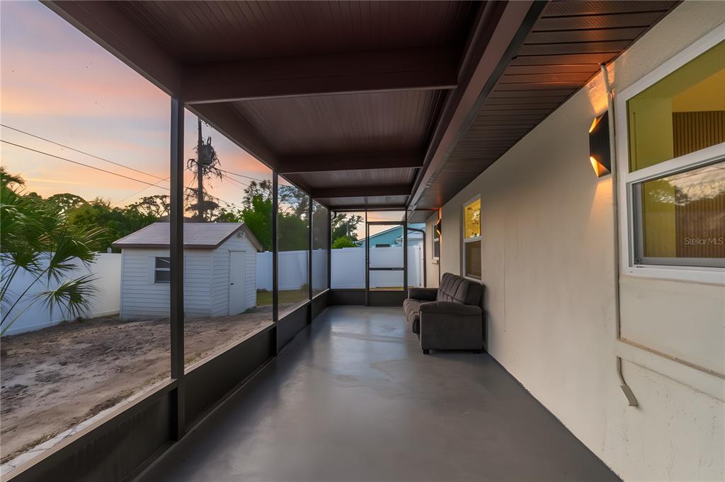 A covered screened-in porch features a gray concrete floor, a sofa, and a backyard view — 1461 ROYAL ROAD, VENICE, FL