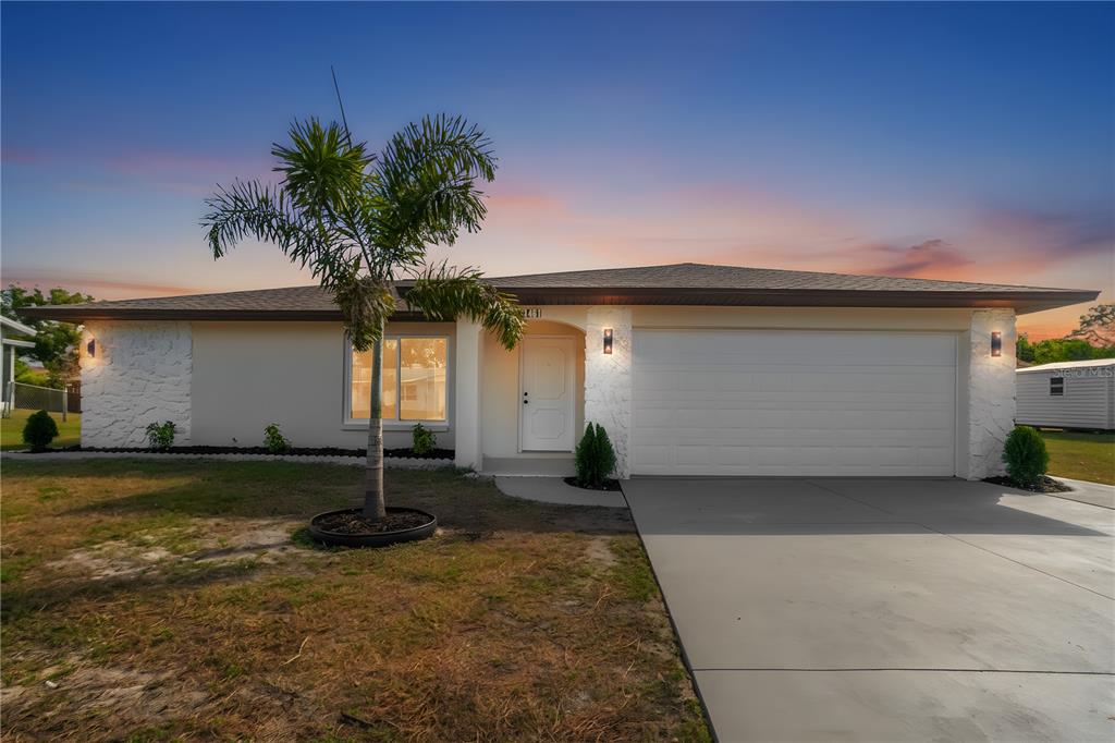 A single-story house with a white stucco facade, stone accents, a palm tree, and driveway — 1461 ROYAL ROAD, VENICE, FL