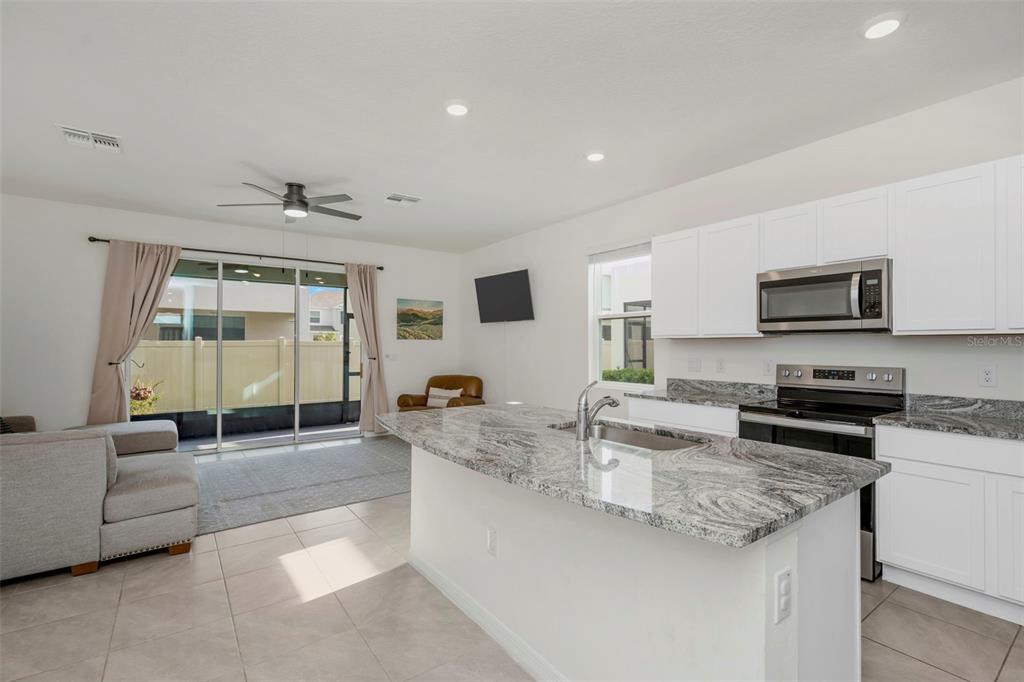 A kitchen with granite countertops and white cabinets overlooks a living area with sliding doors — 17226 AMBER ASPEN WAY, LAND O LAKES, FL