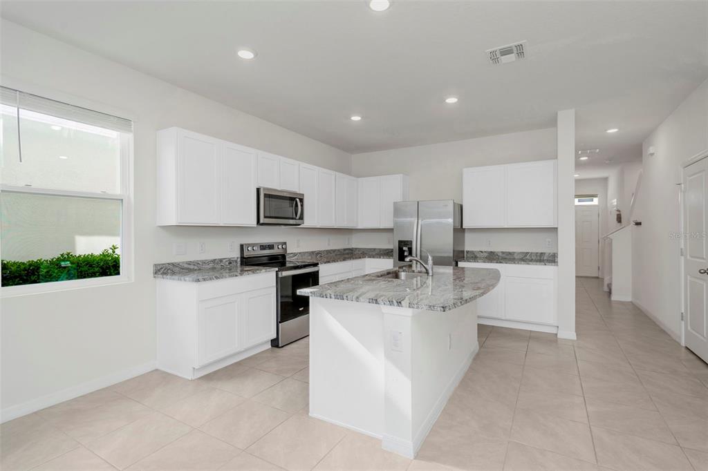 A modern kitchen features white cabinets, granite countertops, a center island, and stainless steel appliances — 17226 AMBER ASPEN WAY, LAND O LAKES, FL