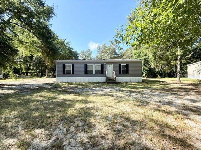 A single-story manufactured home with gray siding sits on a large, grassy, wooded lot — 877 SE 38 WAY, MELROSE, FL