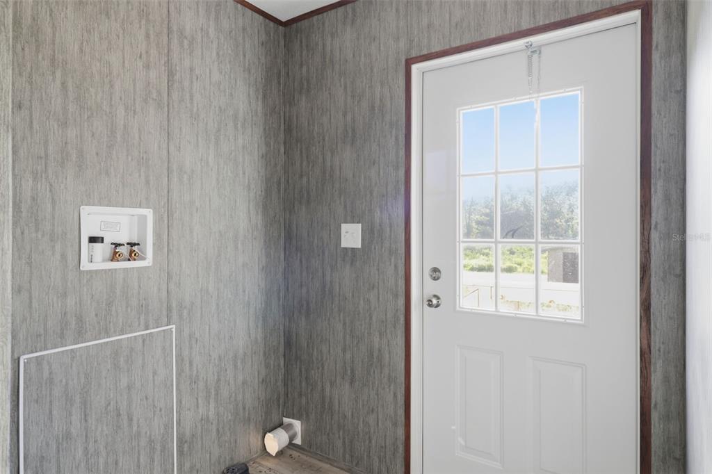 A laundry room with gray wood-look walls, a white exterior door, and washer hookups — 18422 MOORHAVEN DRIVE, SPRING HILL, FL