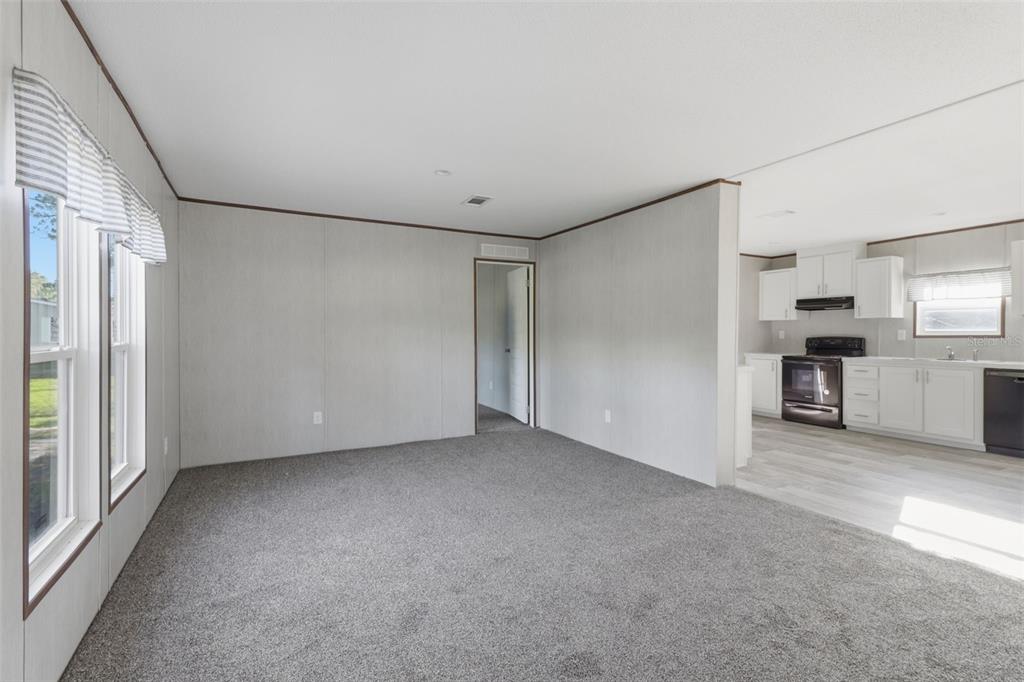A carpeted living room opens into a kitchen with white cabinets and light flooring — 18422 MOORHAVEN DRIVE, SPRING HILL, FL