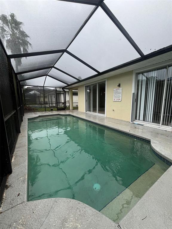 A screened-in swimming pool sits on a concrete patio adjacent to a house with sliding doors — 2915 SUNSET LAKES BOULEVARD, KISSIMMEE, FL