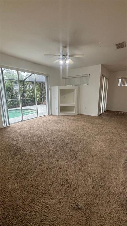 A carpeted living room features a built-in media niche, ceiling fan, and sliding glass doors — 2915 SUNSET LAKES BOULEVARD, KISSIMMEE, FL