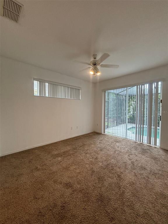An empty room with brown carpet, a ceiling fan, and sliding glass doors to a pool — 2915 SUNSET LAKES BOULEVARD, KISSIMMEE, FL