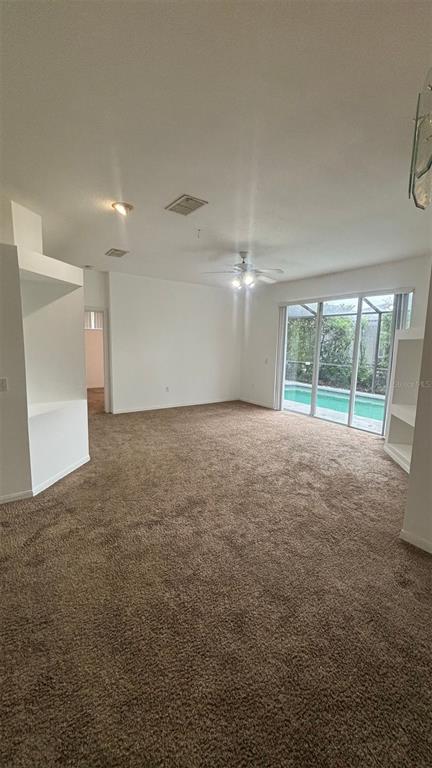 A carpeted living room features a ceiling fan, built-in shelving, and sliding glass doors to a pool — 2915 SUNSET LAKES BOULEVARD, KISSIMMEE, FL
