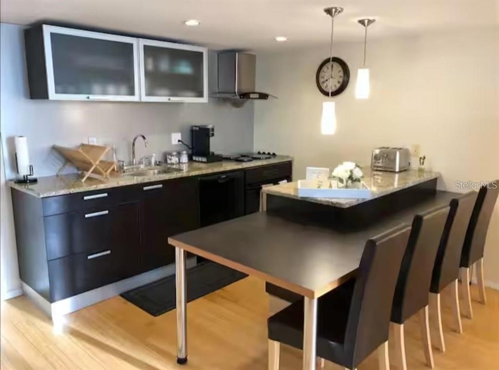 A modern kitchen features dark cabinets, granite countertops, a dining table, and pendant lighting — 701 S MADISON AVENUE UNIT 422, CLEARWATER, FL