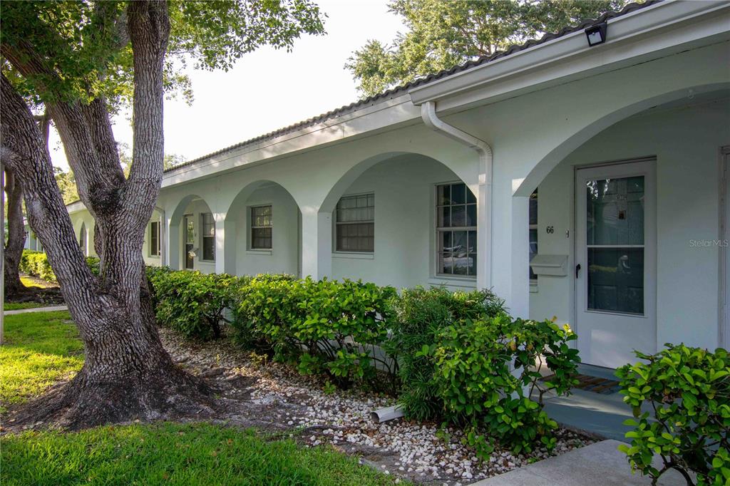 A white building exterior features a covered arched walkway, green shrubs, and a front door — 11200 102ND AVENUE UNIT 66, SEMINOLE, FL