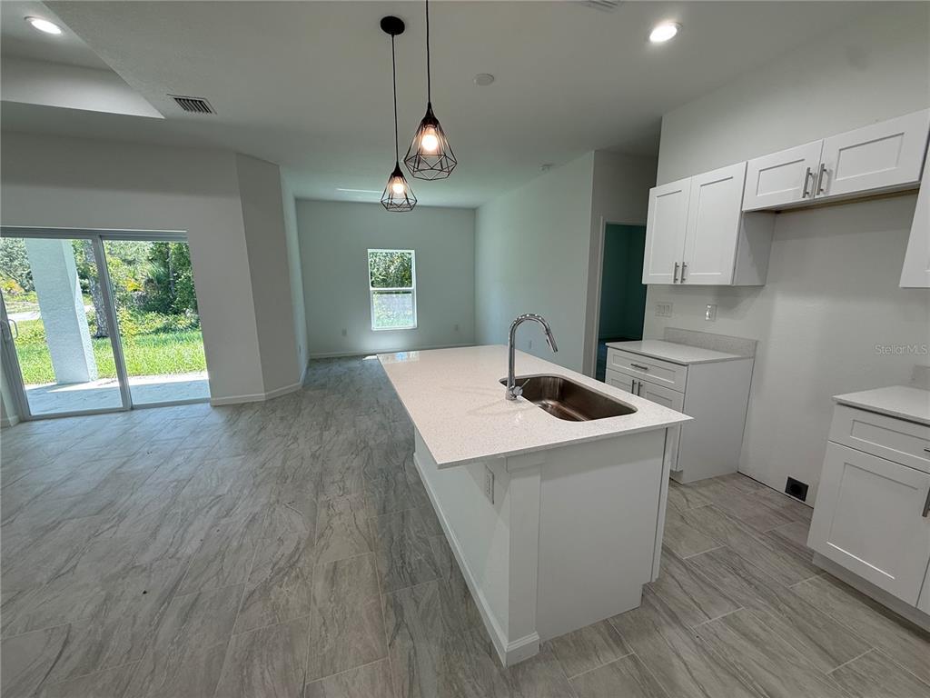 A kitchen features a white island with a sink, pendant lighting, and light-colored tile flooring — 1392 ALABELLE LANE, NORTH PORT, FL