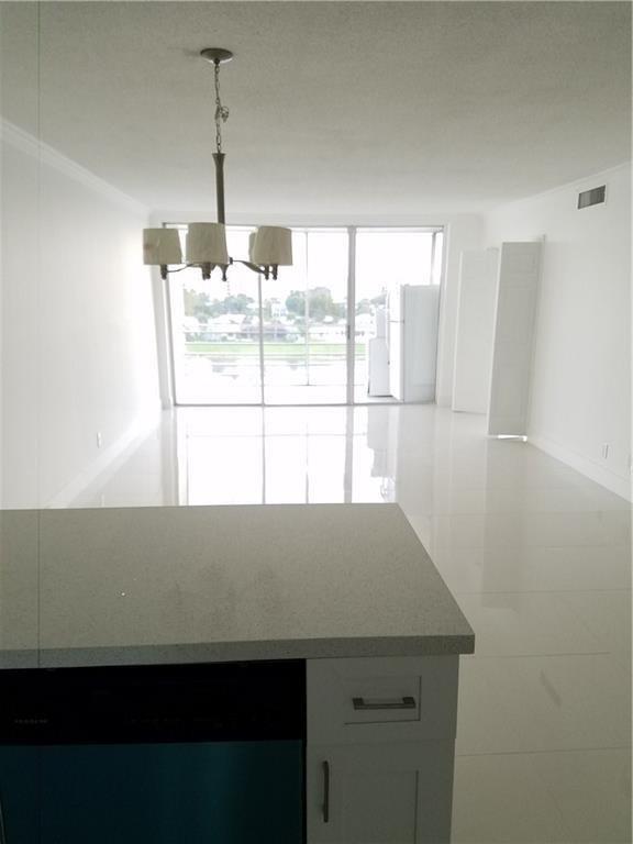 A kitchen island overlooks a bright, open-concept living area with white tile floors and balcony — 3150 N Course Lane # 607, Pompano Beach FL 33069, POMPANO BEACH, FL