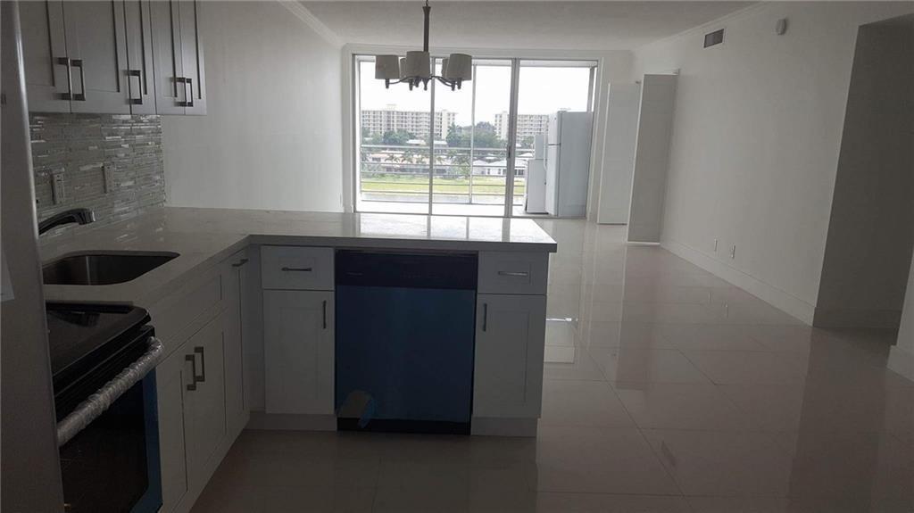 A kitchen with white cabinets and a dishwasher overlooks a balcony with an outdoor view — 3150 N Course Lane # 607, Pompano Beach FL 33069, POMPANO BEACH, FL