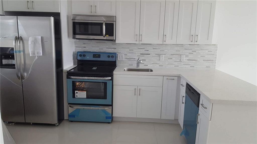 A modern kitchen features white cabinets, stainless steel appliances, and a tiled backsplash — 3150 N Course Lane # 607, Pompano Beach FL 33069, POMPANO BEACH, FL