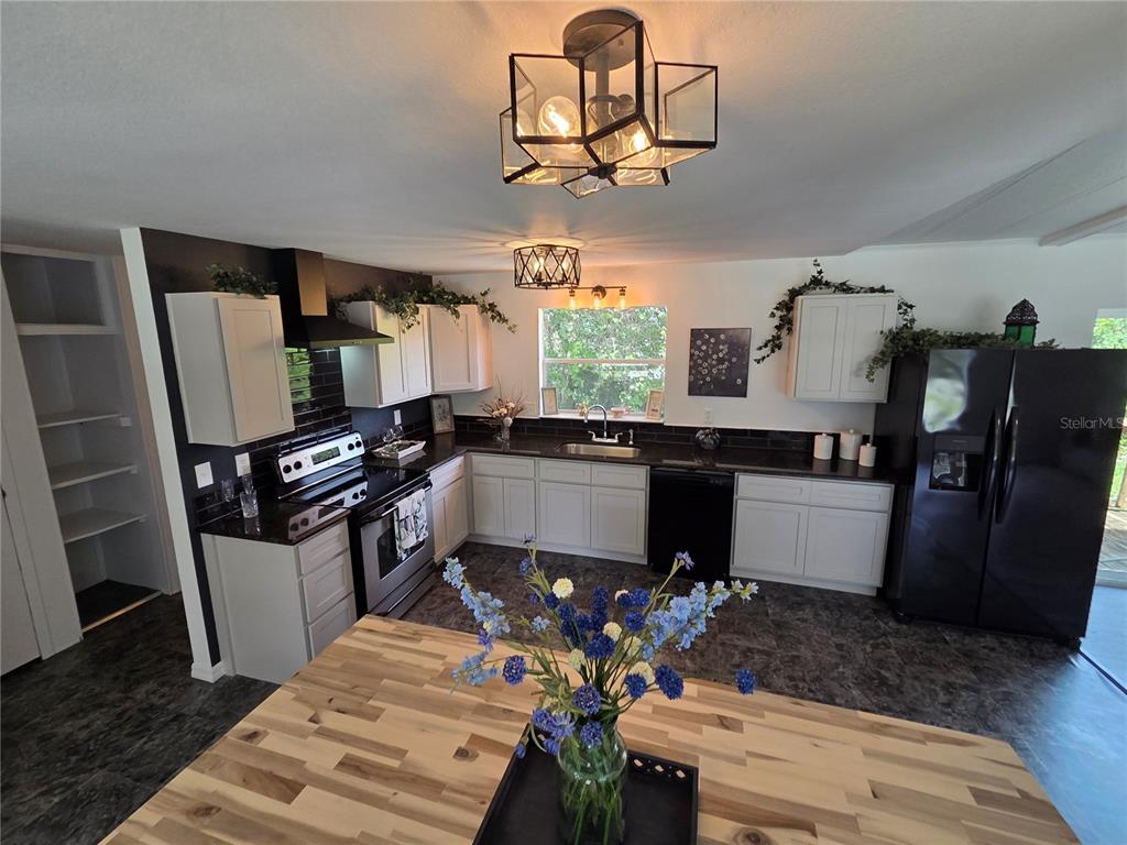 A kitchen features white cabinets, black countertops, stainless steel appliances, and a wooden island — 47807 STATE ROAD 19, ALTOONA, FL