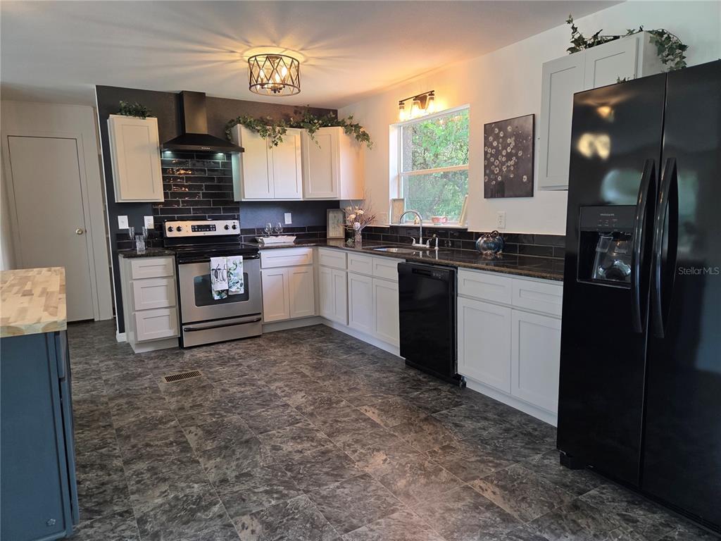 A kitchen features white cabinets, black countertops, a black subway tile backsplash, and dark flooring — 47807 STATE ROAD 19, ALTOONA, FL
