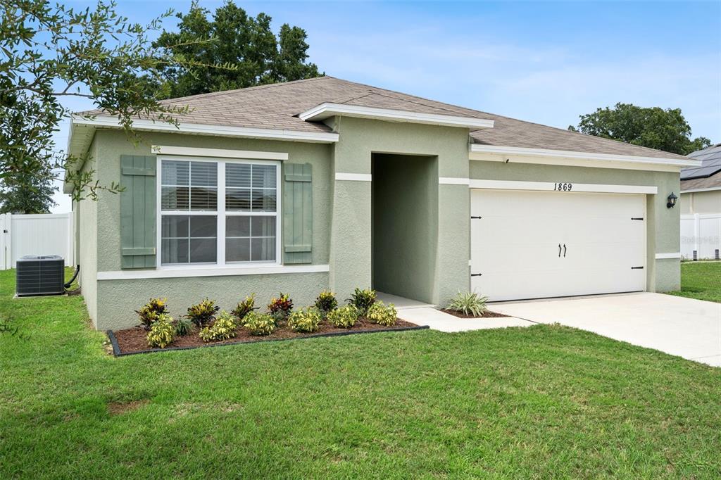 A single-story house with light green stucco siding, a two-car garage, and a front lawn — 1869 SUNSET RIDGE DRIVE, MASCOTTE, FL
