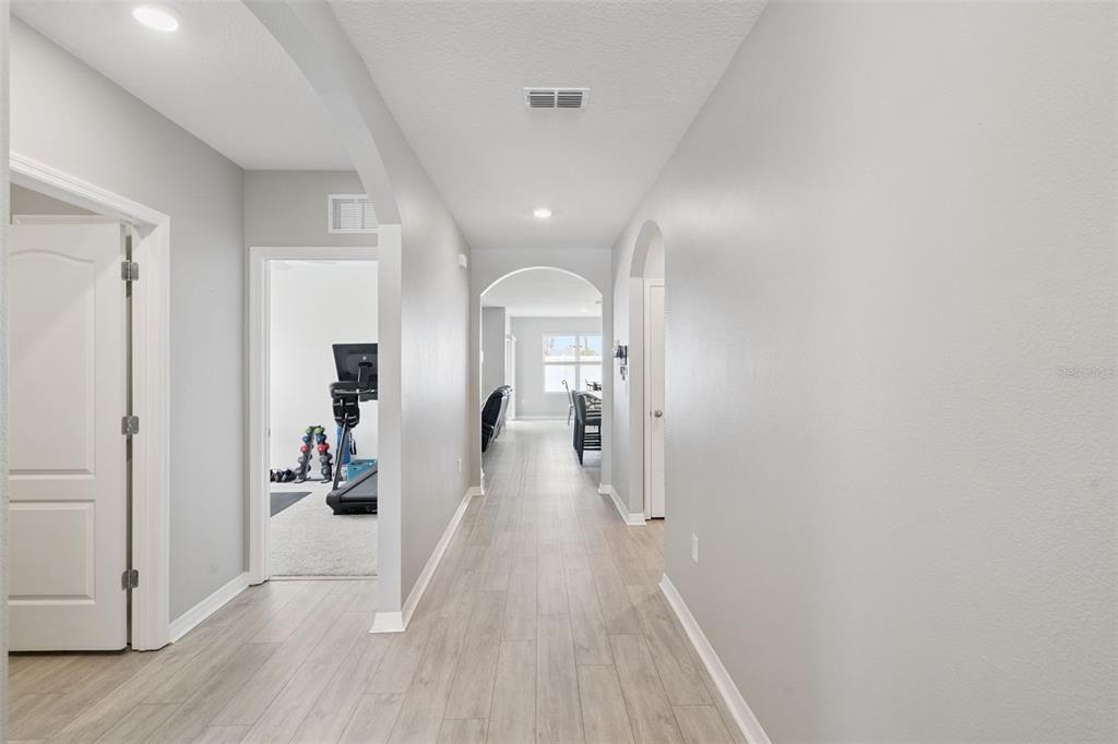 A hallway with light wood-look flooring leads to an arched opening and a home gym — 1869 SUNSET RIDGE DRIVE, MASCOTTE, FL