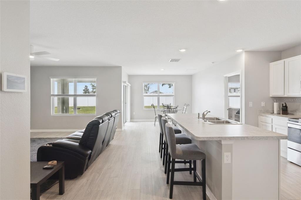An open-concept kitchen and living area features light wood flooring, white cabinetry, and a breakfast bar — 1869 SUNSET RIDGE DRIVE, MASCOTTE, FL