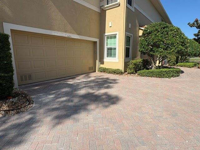 A beige house features a two-car garage and a paved driveway with landscaping — 1425 EMERALD DUNES DRIVE UNIT 17, SUN CITY CENTER, FL