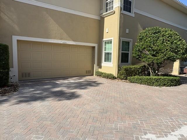 A beige house exterior features a large garage door and a manicured tree in front — 1425 EMERALD DUNES DRIVE UNIT 17, SUN CITY CENTER, FL