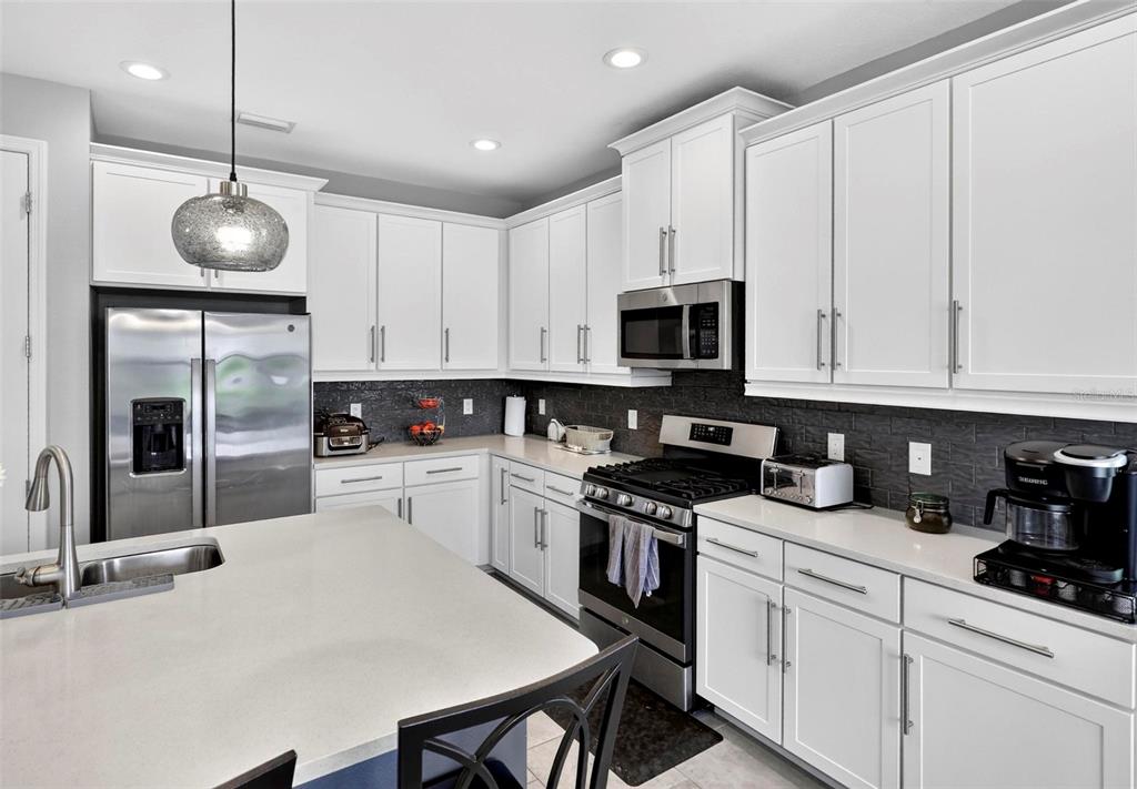 A modern kitchen features white cabinets, stainless steel appliances, a kitchen island, and dark backsplash — 3073 MOUNTAIN SPRUCE TERRACE, WESLEY CHAPEL, FL