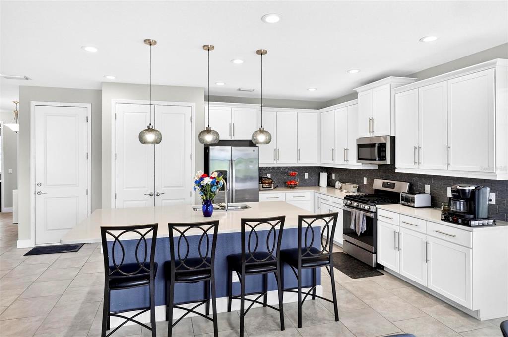 A kitchen features white cabinetry, a blue island with bar seating, and stainless steel appliances — 3073 MOUNTAIN SPRUCE TERRACE, WESLEY CHAPEL, FL