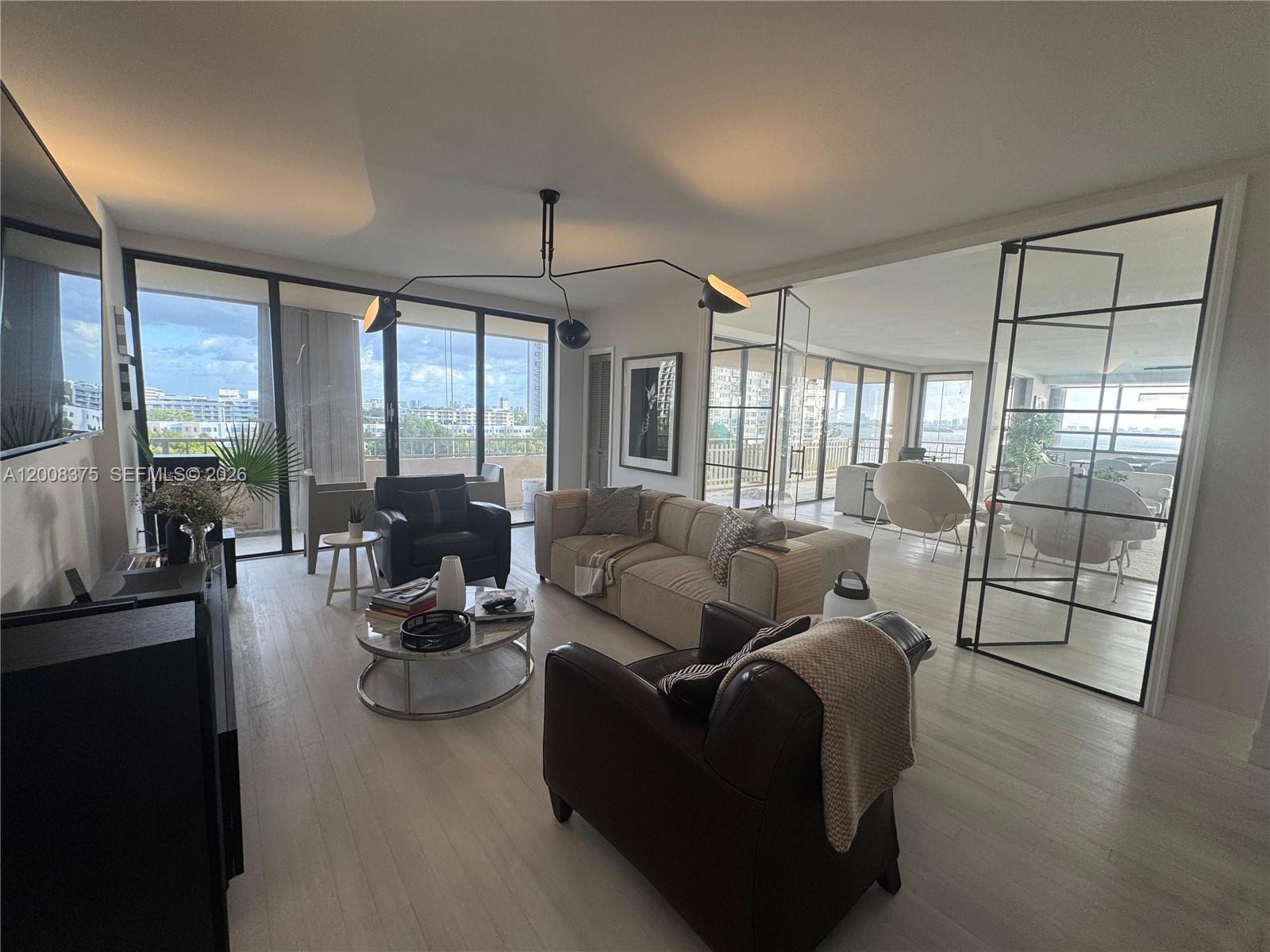 A living room features light wood floors, a modern chandelier, and glass-paneled room dividers — 11113 Biscayne Blvd # 558, Miami FL 33181, MIAMI, FL