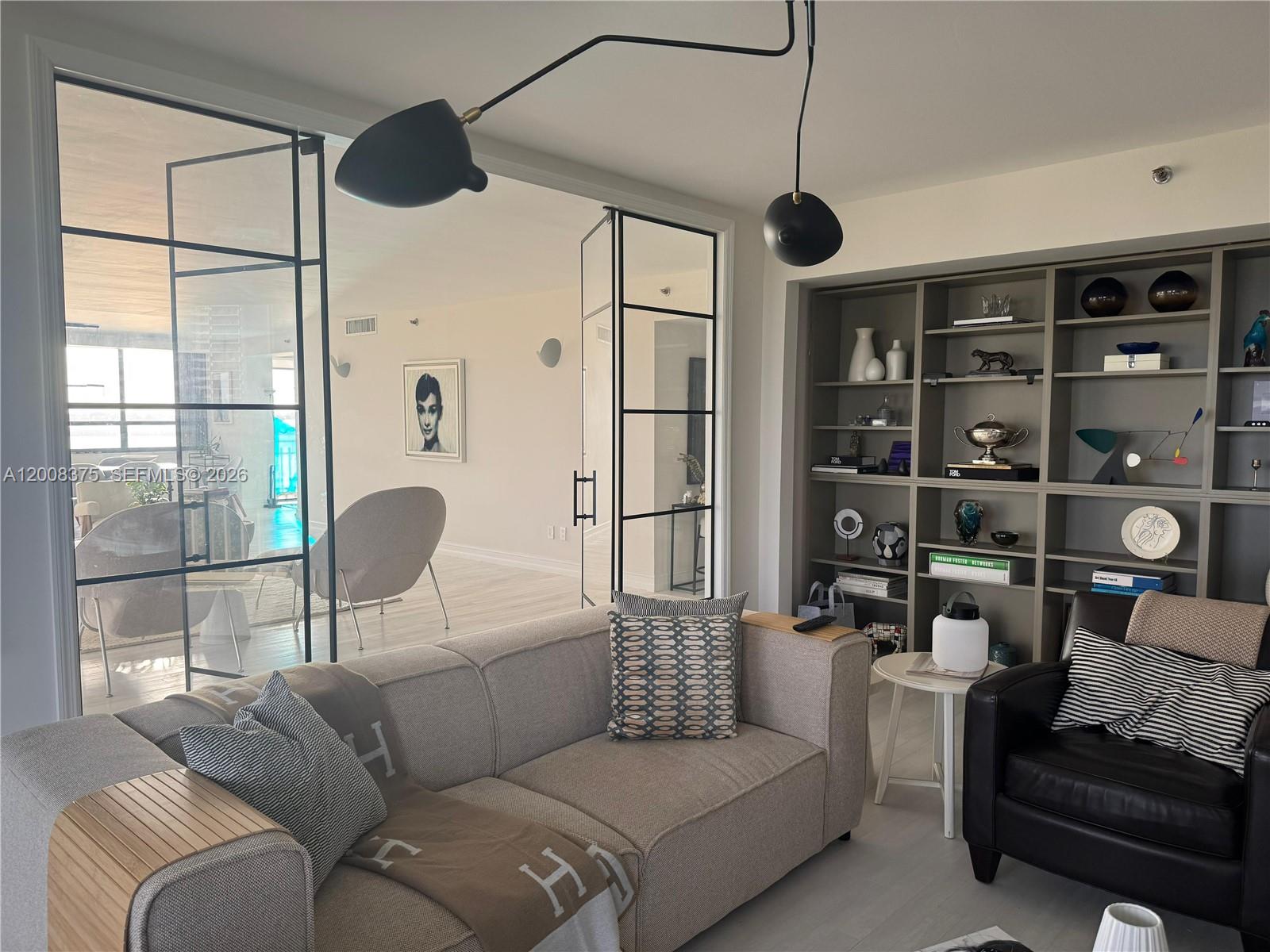 A living room features a beige sofa, a black leather chair, and a glass-paneled room divider — 11113 Biscayne Blvd # 558, Miami FL 33181, MIAMI, FL