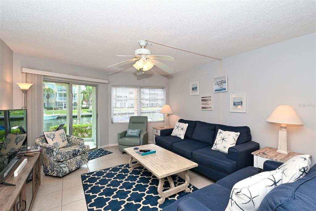 A living room features blue sofas, a patterned armchair, a coffee table, and sliding glass doors — 1257 S PORTOFINO DRIVE UNIT 36, SARASOTA, FL
