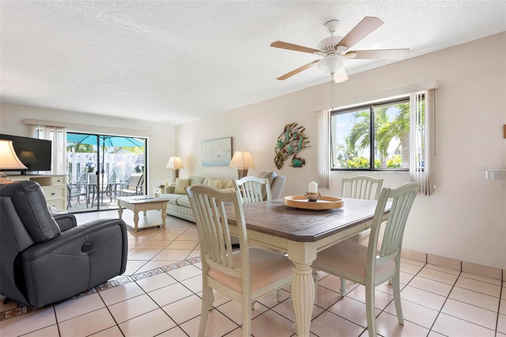 A dining area and living room with tile floors, a ceiling fan, and sliding glass doors — 6703 MIDNIGHT PASS ROAD UNIT 101, SARASOTA, FL