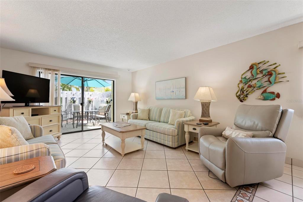 A living room features tile flooring, a striped sofa, a recliner, and a sliding glass door — 6703 MIDNIGHT PASS ROAD UNIT 101, SARASOTA, FL