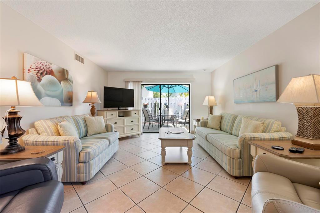 A living room features two striped sofas, a coffee table, and a sliding glass door — 6703 MIDNIGHT PASS ROAD UNIT 101, SARASOTA, FL