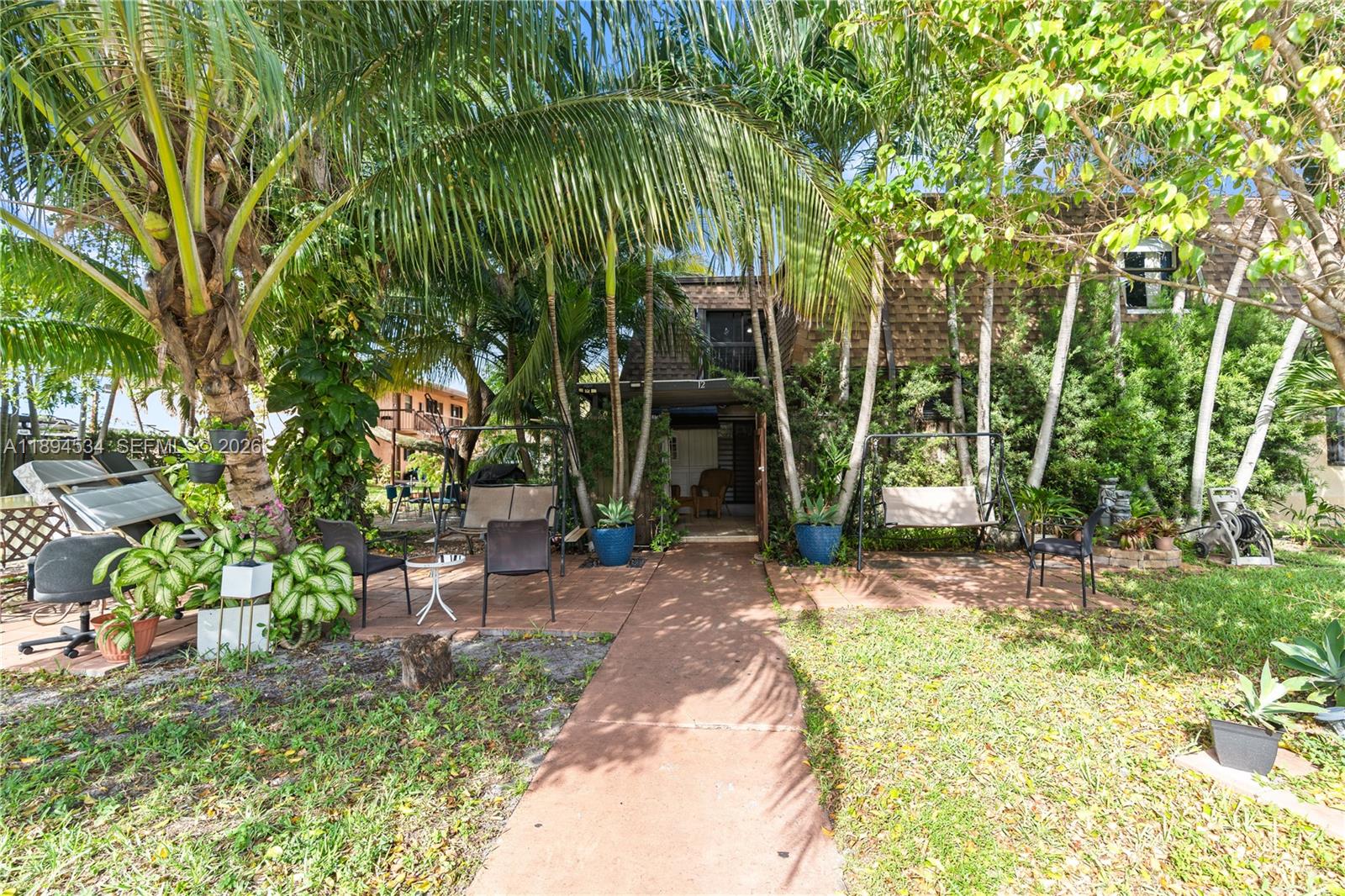 A paved walkway leads to a shaded patio area with outdoor seating and palm trees — 2450 W 67th Pl # 12, Hialeah FL 33016, HIALEAH, FL