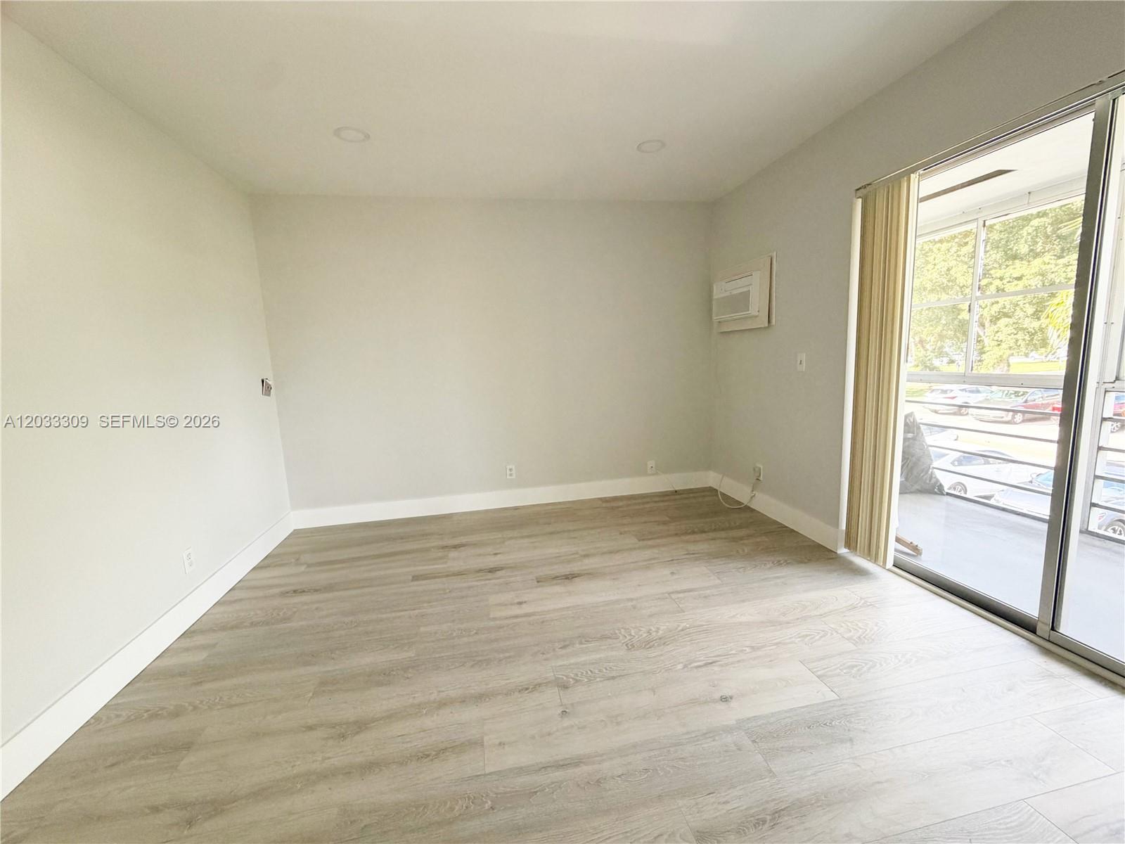 An empty room features light-colored wood-look flooring, white walls, and a sliding glass balcony door — 178 Durham C # 178, Deerfield Beach FL 33442, DEERFIELD BEACH, FL