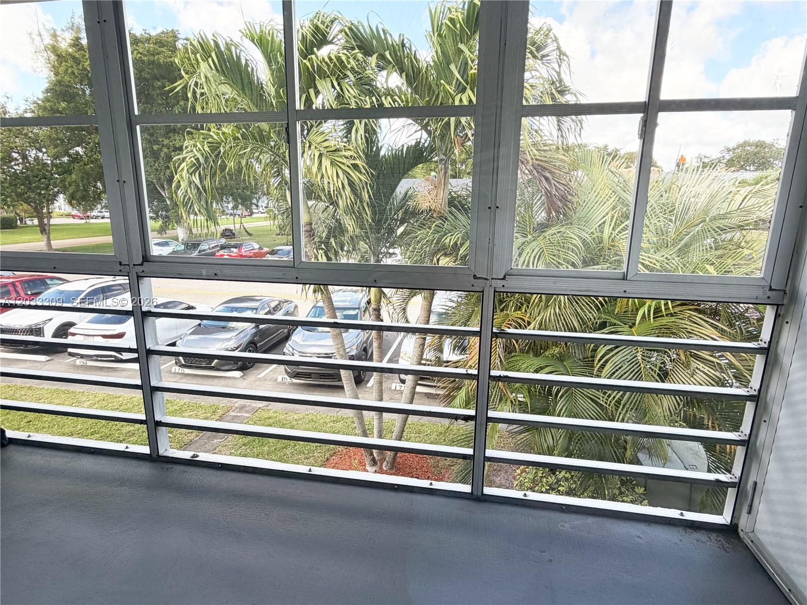A screened-in balcony overlooks a parking lot with several cars and palm trees — 178 Durham C # 178, Deerfield Beach FL 33442, DEERFIELD BEACH, FL