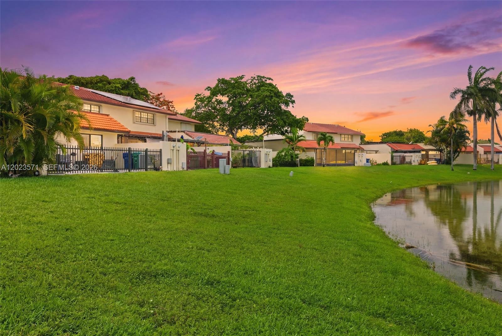 A row of houses with red tile roofs overlooks a grassy lawn and a pond — 19009 NW 64th Ct, Hialeah FL 33015, HIALEAH, FL