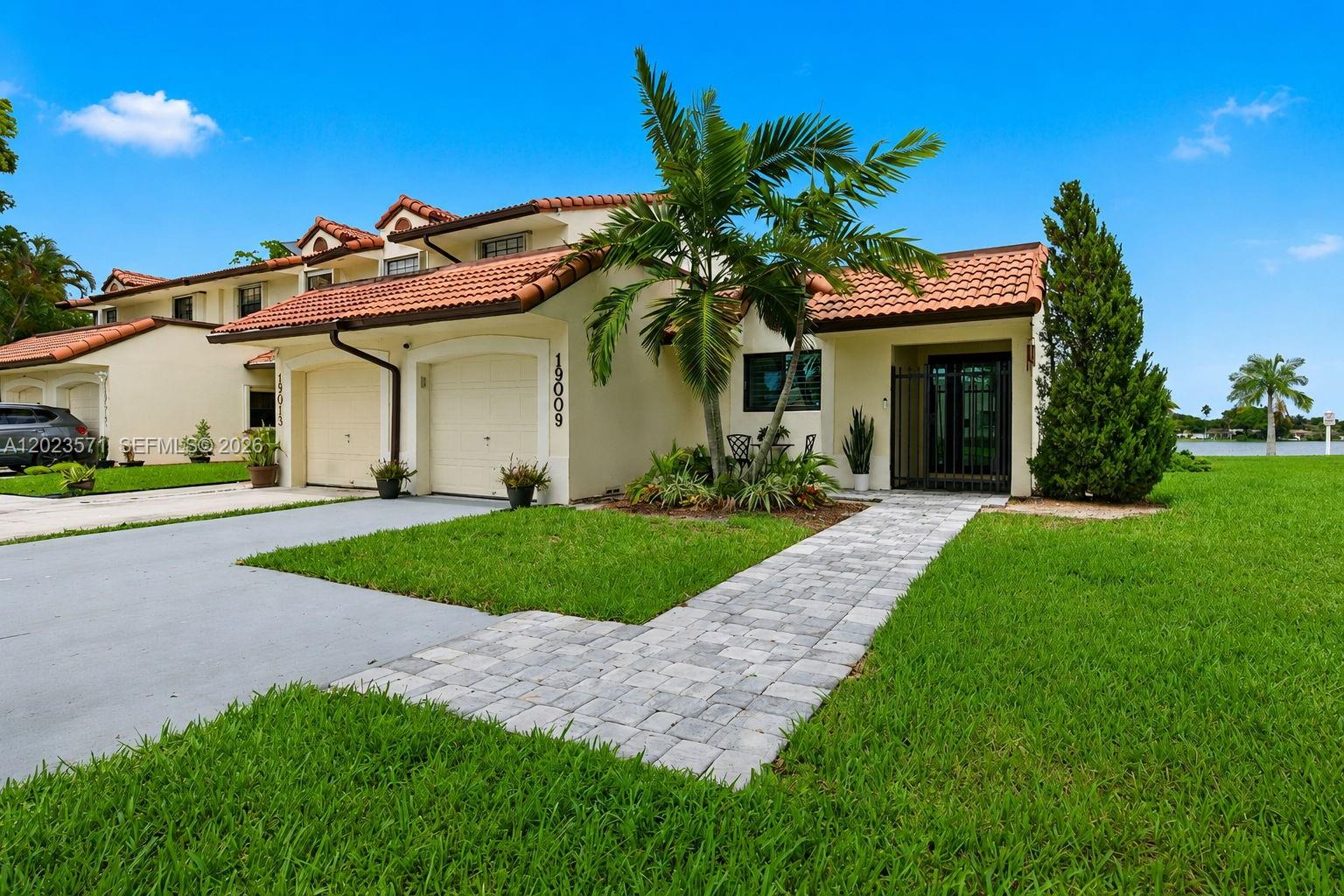 A two-story townhouse with a tiled roof, garage, and a paved walkway leading to the entrance — 19009 NW 64th Ct, Hialeah FL 33015, HIALEAH, FL