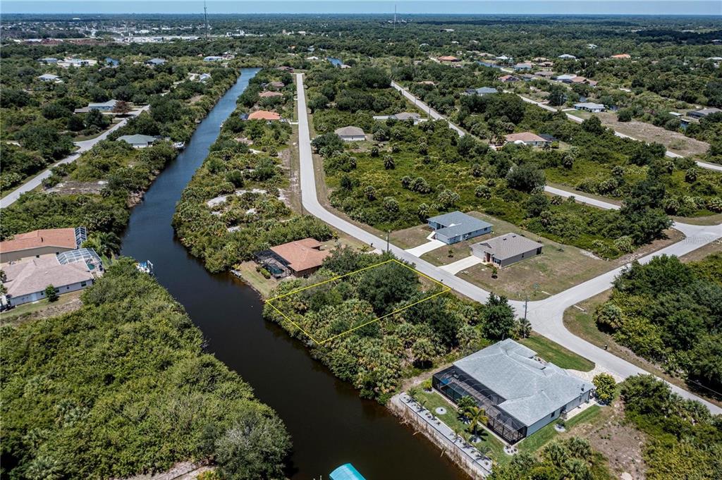 An aerial view shows a vacant, rectangular waterfront lot outlined in yellow near a canal — 13958 ALLAMANDA CIRCLE, PORT CHARLOTTE, FL