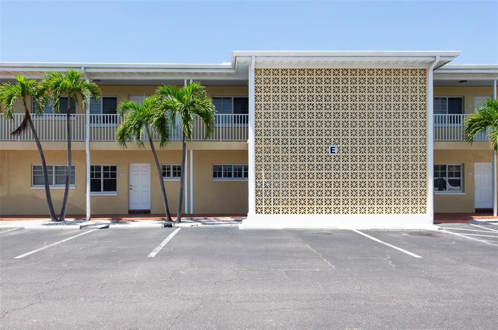 The exterior of a two-story apartment building features a decorative screen wall marked with an E — 19417 GULF BOULEVARD UNIT E109, INDIAN ROCKS BEACH, FL