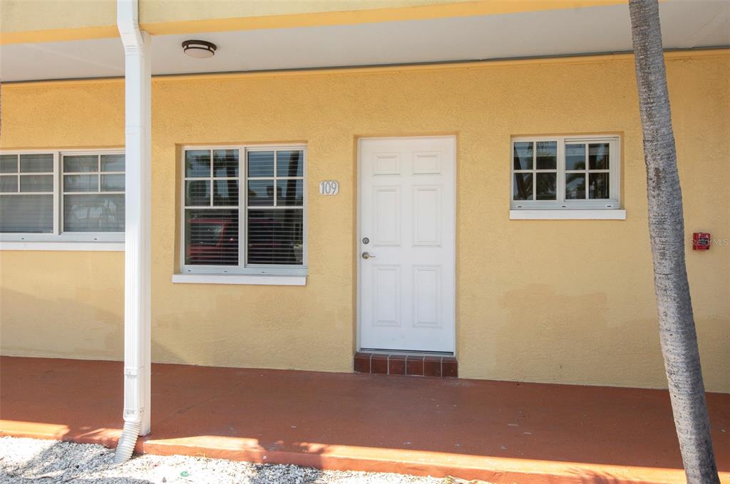 The exterior of a yellow building features a white door, two windows, and a porch — 19417 GULF BOULEVARD UNIT E109, INDIAN ROCKS BEACH, FL